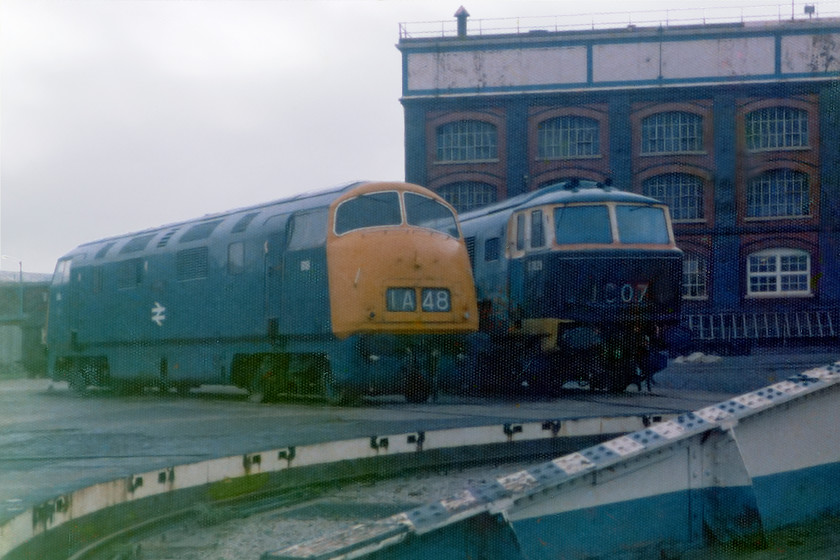 D818 & D7029, turntable, Swindon Works 
 A familiar scene to many who passed on the adjacent GWML was the presence of two of Swindon's finest on display behind the works turntable. 818 'Glory' was a static exhibit that languished on until it was eventually cut up in 1985. 7029 had a slightly happier story to tell. The Diesel Traction Group owned the engine when this picture was taken at Swindon and were preparing it for overhaul. Since then it has worked extensively on the preserved network and, at the time of writing, is based at the Severn Valley Railway where it is a regular performer. 
 Keywords: Swindon Works turntable Warship D818 Glory Hymek 7029