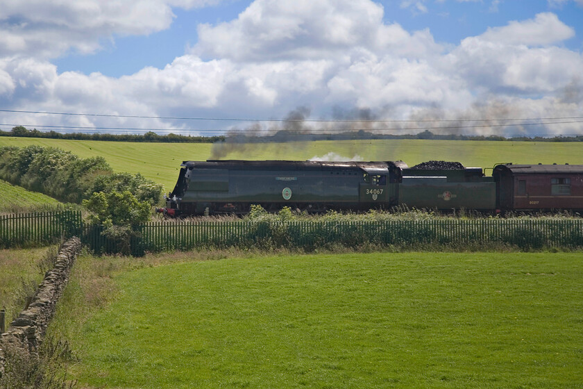 34067, outward leg of The Cumbrian Mountain Express, 06.30 London Euston-Carlisle (1Z86, 36L), Sedgwick SD514861 
 A green locomotive in a green landscape and against the sun; what a photographic disaster! I had identified this spot on the OS map to photograph The Cumbrian Mountain Express charter led by 34067 'Tangmere' but from a footpath on the other side of the line as seen behind the locomotive. However, I misjudged the time it would take us to get here near the village of Sedwick from Arnside given a traffic jam in the village of Milnthorpe and finally the lack of anywhere to park the car on the narrow lanes. With the train, running as usual as 1Z86, having already started its assault of Shap this wrong-side shot had to suffice. Some Photoshop manipulation has helped improve things but it is rather a poor shot. 
 Keywords: 34067 The Cumbrian Mountain Express 06.30 London Euston-Carlisle 1Z86 Sedgwick SD514861 Tangmere