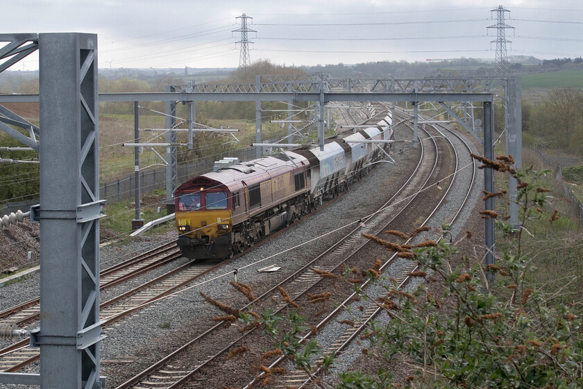 66093, 08.58 Elstow Redland Sidings-Mountsorrel Sidings (6D32, 21E), Irthlingborough Road bridge 
 This looks to be a terrible photograph and, it is! However, I took it to remind myself of what a superb spot this used to be from Wellingborough's Irthlingborough Road bridge. For years it was the 'go to' spot for many local photographers due to its wide open and sweeping vistas, in both directions. However, the ridiculously over-engineered bridge, the palisade fencing, the electrification paraphernalia and now lineside growth (in this case buddleia) have conspired to make it worse than useless! 66093 approaches on the down slow line with the 08.58 Elsow Redland Sidings to Mountsorrel empty stone train running as 6D32. 
 Keywords: 66093 08.58 Elstow Redland Sidings-Mountsorrel Sidings 6D32 Irthlingborough Road bridge EWS