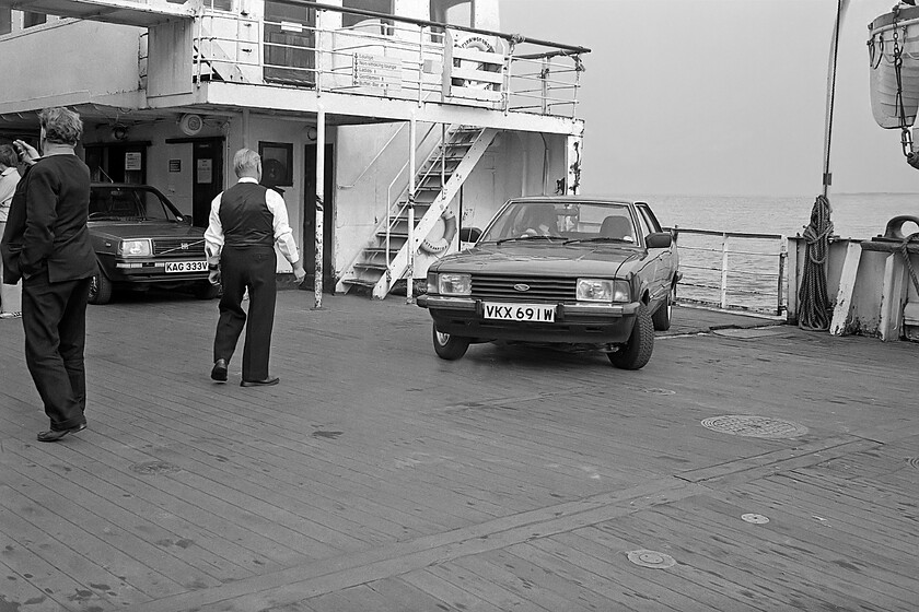 Unloading MV Farringford, Hull Corporation Pier 
 Vehicle unloading from MV Farringford at Hull Corporation Pier continues apace under the guidance of the ship's crew. In this view, the driver of the Luton registered Ford Cortina gingerly reverses in order to come forwards and cross the side loading bulwark to join the floating pontoon pier, to then proceeed up the loading ramp and on to dry land. The driver of the locally registered (Hull) Volvo 343 could be next off. Of the two cars, the Volvo only lasted until 1986 outlived by the Cortina which was last on the road in 1989. However, the MV Farringford, from which they are disembarking, was to come out of service a week after this photograph was taken and only lasted for another three years cut up locally at Silcock's Basin in 1984 after a failed attempt to sell it for future use in Scotland. 
 Keywords: Unloading MV Farringford, Hull Corporation Pier Ford Cortina Volvo 343