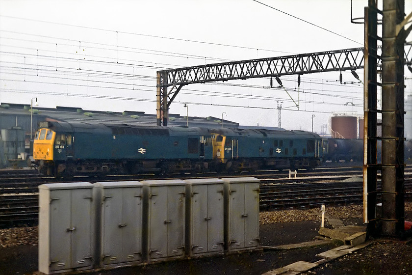 25161 & 24035, stabled, Crewe Diesel Depot 
 As we came into Crewe all eyes were to the left of the train as we passed Crewe Diesel Depot. The Exa camera did a good job at capturing what was about given its slow shutter speed and the waist-level viewfinder I was forced to use; difficult out of a train window at speed! Here 25161 and 24035 seen stabled on the depot. The 25 was withdrawn in 1981 only to be reinstated 'til 1984. The class 24 had another year in service being withdrawn in November 1978. 
 Keywords: 25161 24035 Crewe Diesel Depot