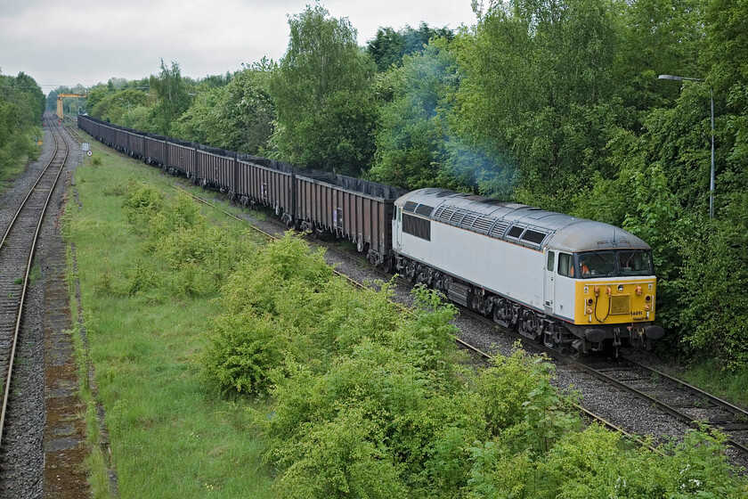 56091, after unloading flyash, site of Calvert station 
 With the unloading of the flyash complete 56091 creeps away past the vergroen remains of Calvert station. The 56 will then take part in some train Tetris where it runs round and reverses the train around a torturous curve on to the remains of the Varsity Line where it will then run round again to lead the train back to Didcot again. Notice the yellow crane in the background. This has been used in the past to unload the containers that have been brought to this site full of rubbish to be buried in the huge quarry close by. 
 Keywords: 56091 site of Calvert station flyash DCR