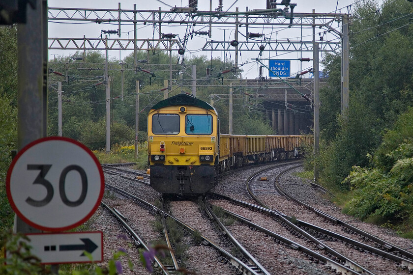 66593, 09.14 Bescot Yard-Bromford Bridge (6Y60, 30L), Bescot Stadium station 
 66593 '3MG Mersey Multimodal Gateway' is towed at the rear of the 6Y60 09.14 Bescot Yard to Bromford Bridge engineering train seen from Bescot Stadium station. After the late arrival of this locomotive and the leading one, 66587 'As One We Can', in from Basford Hall this train left over thirty minutes late. Its seventeen-mile circular route to its destination took it all the way back south right into the chaotic HS2 work zone near Castle Bromwich. Notice the signage on the elevated M6 motorway above the train. 
 Keywords: 66593 09.14 Bescot Yard-Bromford Bridge 6Y60 Bescot Stadium station 3MG Mersey Multimodal Gateway