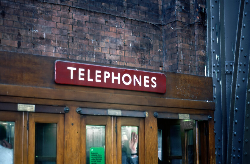 Enamel, London St. Pancras station 
 A lovely period line of telephone boxes is seen inside St. Pancras station complete with a British Railways (London Midland) enamel. In the days before mobile 'phones and other forms of personal mass communication public facilities such as this were extensive and found at most stations in long lines or blocks. I am not at all sure what the man in the middle kiosk is doing, perhaps taking in a little spotting whilst making his call? 
 Keywords: Enamel London St. Pancras station BR London Midland