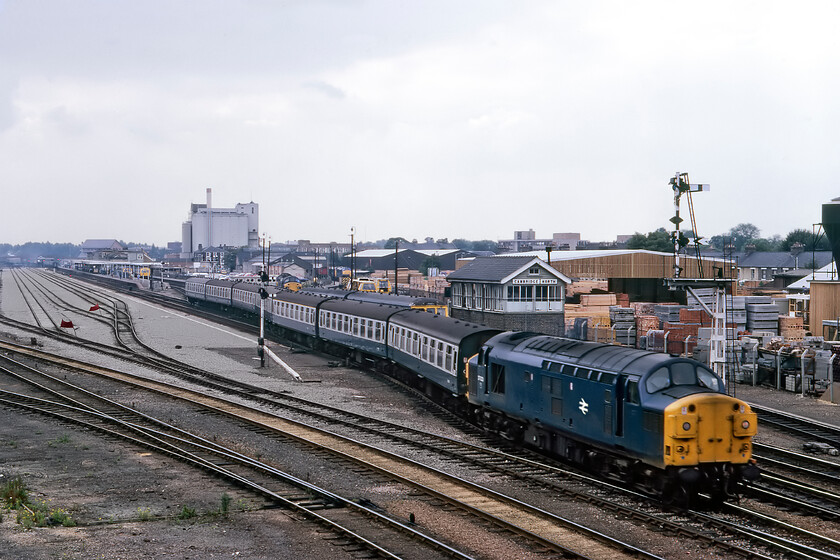 37028, 14.05 London Liverpool Street-Cambridge (2L85) ECS, Cambridge North 
 Having just arrived with the 2L85 14.05 from Liverpool Street 37028 eases the empty coaching stock out of Cambridge station to go off to the carriage sidings for servicing. Notice the huge and extensive new complex of sidings to the left that are not yet in use indicated by the red flags draped across the tracks. Their installation was part of the modernisation of the Cambridge area that included resignalling thus sealing the fate of Cambridge North box seen to the right. Ultimately, in 1988, the electrification of the area was completed changing this scene, taken from Mill Road bridge, substantially. The split box Class 37 led a varied life including being one of a number sent to France for work with Fertis ending its life at EMR in Kingsbury in the winter of 2008. 
 Keywords: 37028 14.05 Liverpool Street-Cambridge 2L85 ECS Cambridge North