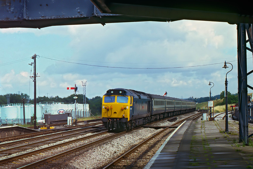 50048, 08.57 London Paddington-Paignton (1B38), Tiverton Junction station 
 On the return ride, I again called in at Tiverton Junction. With the rail connected oil terminal in the background, 50048 'Dauntless' takes the centre road with the 08.57 London Paddington to Paignton. However, I am not convinced, forty years on, that this is actually this working as I believe that this was not usually composed of Mk. II stock and fifty hauled. This station oozed GW character and I made a number of very enjoyable visits right up to and after it closed. Also, note the truncated siding to the far right with the embankment of the M5 motorway beyond it. This was the former Hemyock branch line that closed to passengers in September 1963 but stayed operational for access to the creamery until October 1975, with the construction of the M5 causing the line to be cut. 
 Keywords: 50048 08.57 London Paddington-Paignton 1B38 Tiverton Junction station