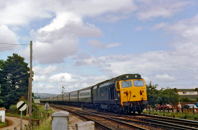 50038, 12.23 London Paddington-Penzance, Stoke Canon crossing 
 The small village of Stoke Canon once boasted a station that closed on 13th June 1963. The signal box was located at the level crossing that was just behind me to my right. 50038 'Formidable' approaches the level crossing with the 12.23 London Paddington to Penzance sweeping into the reverse curve. In classic style, the two children on the far side of the line, out on their bikes with their gran. watch the train pass. Just behind them is a large blue unidentifiable 1960's car of some kind along with a far more familiar red two-door Triumph Herald. 
 Keywords: 50038 12.23 London Paddington-Penzance Stoke Canon crossing