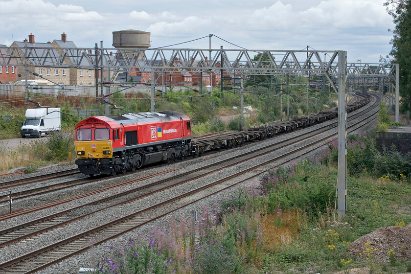 66099, 12.19 Tilbury-Trafford Park (4M85, 9E), site of Roade station 
 66099 still looks smart as it passes the site of Roade station in its recently applied DB Cargo UK livery that it received back in the spring. The 66 is leading the 4M85 12.19 Tilbury to Trafford Park which was composed entirely of flats with no boxes in sight. 66099 also wears the Ukrainian flag with the words #WeStandWithUkraine which were unveiled prior to it hauling the first train with humanitarian aid supplies from the UK (over 1,000,000 items weighing 1500 tons in 24 containers on a train that was over 500 metres long) on 14.04.22. 
 Keywords: 66099 12.19 Tilbury-Trafford Park 4M85 site of Roade station