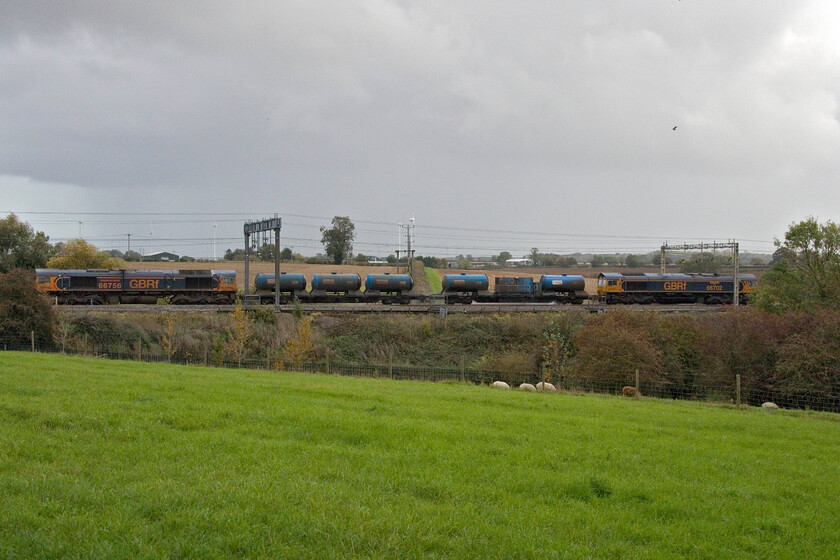 66702 & 66756, 10.30 King's Norton-King's Norton (3J01, 17L), Roade hill 
 It was a gamble that did not quite payout! I had judged that the entire 10.30 King's Norton return RHTT would fit in the gap between the trees between Roade and Ashton and it so nearly did. GBRf's 66702 'Blue Lightning' leads the treatment train with 66756 Royal Corps of Signals bringing up the rear. Notice the resident alpacas grazing in the field. I figured that this would be the last time that I would be able to capture this working as the clocks were to go back on this evening meaning that it would be too dark at its scheduled pass time here. 
 Keywords: 66702 66756 10.30 Kings Norton-Kings Norton 3J01 Roade hill