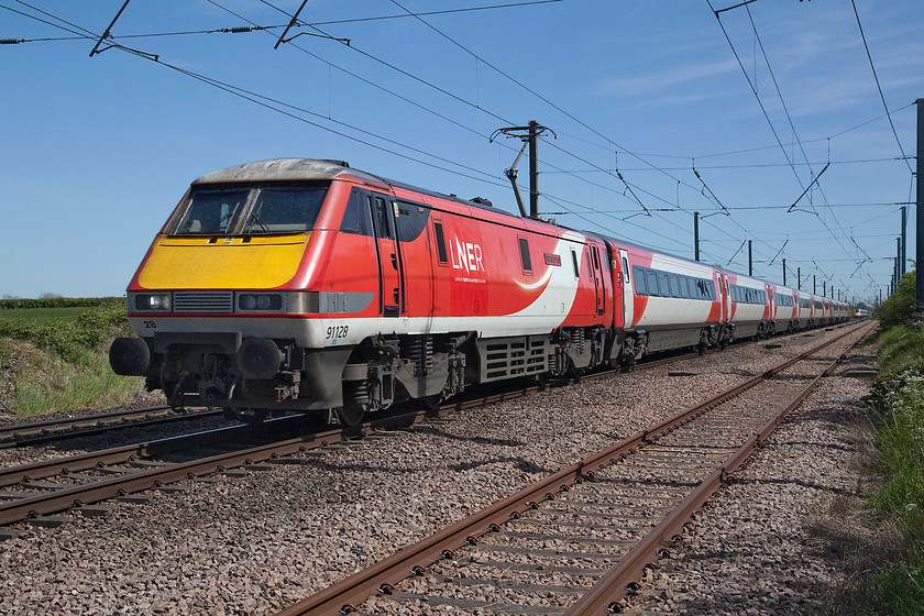 91128, GR 13.30 London King`s Cross-Edinburgh (1S19, 5L), Barnby Lane SK850495 
 91128 'InterCity 50' passes Barnby Lane level crossing, one of three in the village of Claypole, with the 13.30 King's Cross to Edinburgh. It's a feature of the electrification system used on the ECML constructed to a tight budget by BR in the late 1980s, that how high the pantographs extend, this one is not far off the vertical position. Notice the class 800 Azuma heading south in the distance working a press-launch train returning from Leeds to King's Cross. 
 Keywords: 91128 13.30 London King`s Cross-Edinburgh 1S19 Barnby Lane SK850495