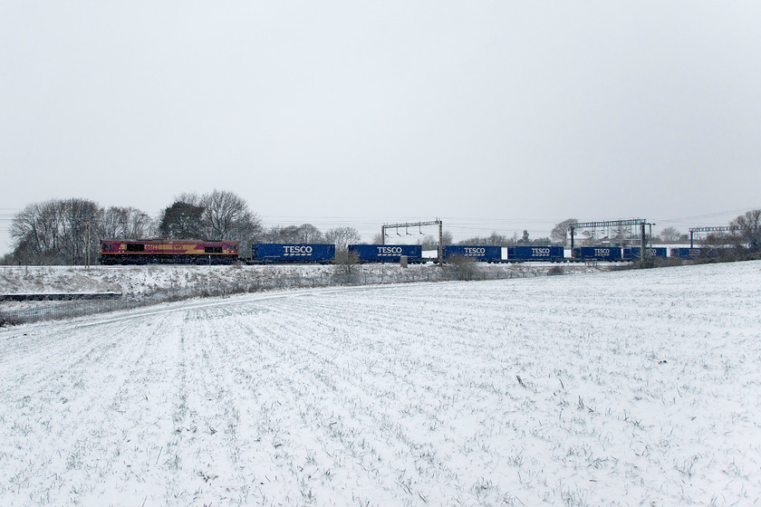 66122, 10.10 DIRFT-Ripple Lane (4L48, 1E), between Roade & Ashton 
 I ran out of time here! Having seen the 4L98 had left Rugby, after initially heading north from Daventry and changing ends, I raced as quickly as I could in snow boots to a spot near to Roade Hill. I wanted to get away from my usual haunts to get a photograph of the train running on the up fast line. However, 66122 hauling the earlier timed 10.10 Daventry to Ripple Lane Tesco Express made better progress than I was able to make so I had to make do with this spot in the middle of a snowy field. GBRf is still struggling with locomotive availability as it is still using hired in Class 66s from DB Cargo, in this case, an example still wearing the defunct EWS livery that it had since arrival in the UK in late 1999. 
 Keywords: 66122,10.10 DIRFT-Ripple Lane 4L48 between Roade & Ashton EWS Tesco Express GBRf