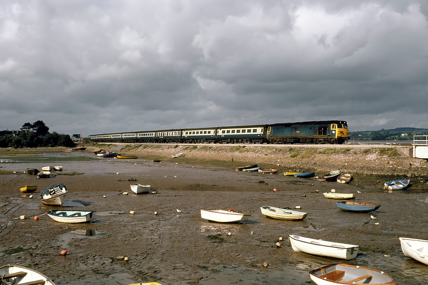 50042, 13.30 Paddington-Paignton (1B84), Cockwood Harbour 
 Back in the days when Cockwood Harbour could be photographed without the scourge of fencing spoiling the view! With an array of small boats sitting on the mud, including one for sale if you call Exeter 66058, 50042 'Triumph' passes leading the 13.30 Paddington to Paignton. 50042's paintwork looks a little faded and was another two years until it got the call to head north to Doncaster for rebuilding. 
 Keywords: 50042 13.30 Paddington-Paignton 1B84 Cockwood Harbour Triumph