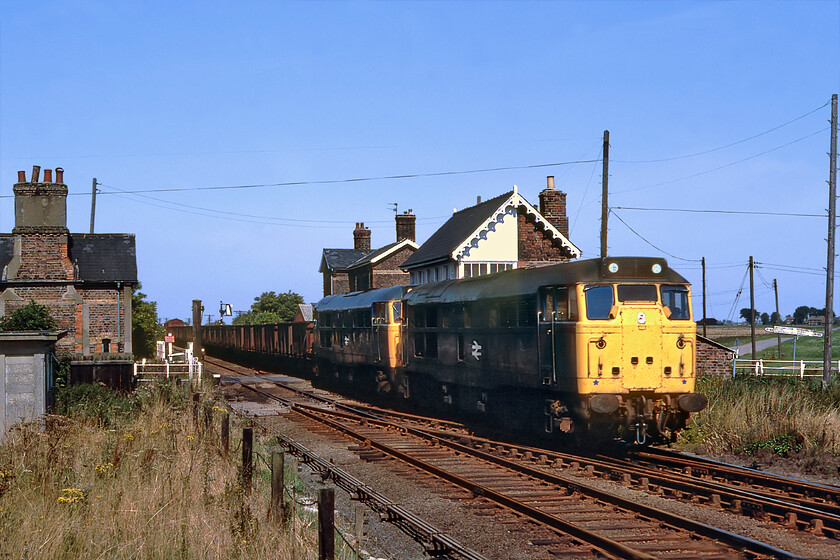 31287 & 31308, up freight, Postland 
 On arrival at Postland whilst retracing yesterday's journey from Spalding to March following the former GE & GN Joint railway the gates were closed and an up train was pegged by the signalman in the superb 1882 Great Northern box. 31287 and 31308 are seen heading south east leading what appears to be a rake of 16T vacuum braked mineral wagons. Trains such as this were becoming increasingly rare on the railways by the early 1980s so it was good to record one here. Today, whilst the station building and the box still stand, even if the latter is in a precarious state, the building to the left has been demolished. 
 Keywords: 31287 31308 up freight Postland