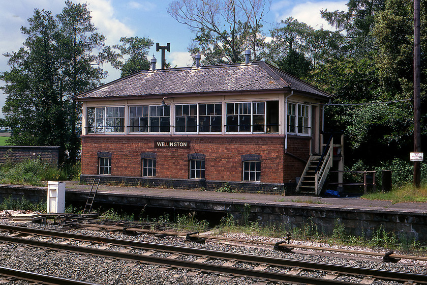 Wellington signal box 
 Wellington signal box, smart with its BR (Western Region) enamel. Notice the strategically placed ladder from the old platform to track level for the signalmans use; health and safety anybody? This box sits on the redundant up platform from which the loop has been removed. The down loop remains in use today and is used by engineering trains. The box is one of the Great Western's standard brick-built Type 7 designs with the classic three panes over two window arrangement. This is a large box with four windows into the frame room and it is a little incongruously squat as it sits on the old station platform. This arrangement is the same as that at Tiverton Junction some eight railway miles to the west. 
 Keywords: Wellington signal box