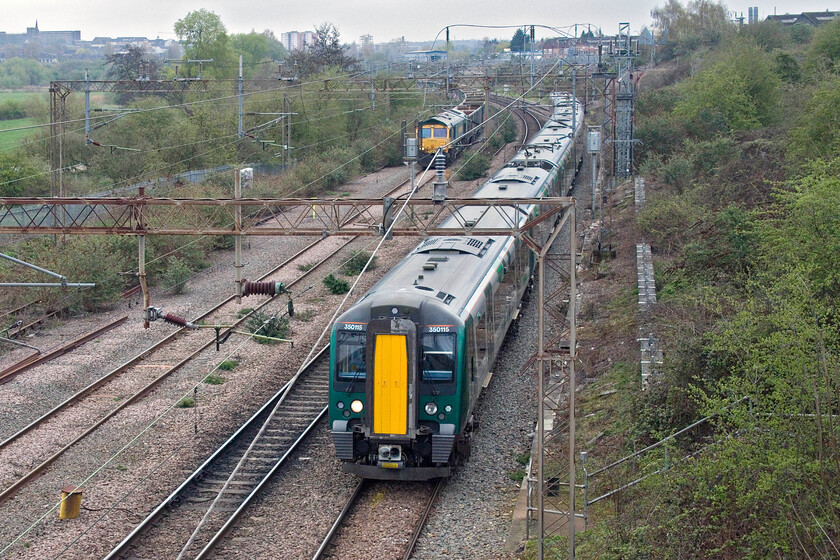 350115, LN 08.56 London Euston-Birmingham New Street (1Y21, 1L) & 66522, 10.22 Northampton Castle Yard-Tunstead Sidings (6Z87, RT), Mill Lane bridge 
 While I have taken a few photographs from Northamptons Mill Lane bridge I have never attempted one from this angle that includes Northamptons skyline in the background. If the sun had been out at this time of day this would have been a tricky position to try as it faces south east so, for once, I bless the clouds! 350115 leads another Desiro on the climb away from Northampton with the 08.56 Euston to Birmingham New Street London Northwestern service. In the background, 66522 waits patiently to get the 6Z87 Northampton Castle Yard to Tunstead Sidings empty stone train away. 
 Keywords: 350115 08.56 London Euston-Birmingham New Street 1Y21 66522, 10.22 Northampton Castle Yard-Tunstead Sidings 6Z87 Mill Lane bridge London Midland Desiro