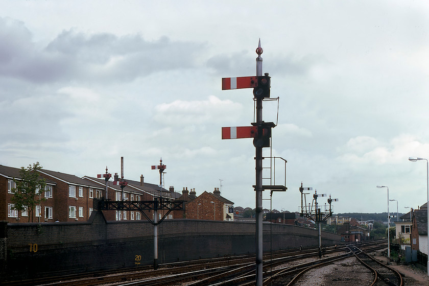 Signalling, High Wycombe station 
 Some of the superb GWR signalling to the east of High Wycombe station. Of particular interest is the lovely gantry of starter signals that is part supported by the railway's retaining wall. Of the original five dolls, three remain and they are all fitted with wooden centre-pivot arms in an effort to save space. Also, notice the rather grand down inner home bracket that supports three dolls all at different heights indicating their relative importance. The highest one to the left (in this view) will be for the down fast line. Notice The Belle Vue pub in the background with its distinctive Watneys sign hanging from the front. Amazingly, this pub is still there on Gordon Road but is now marketed as The BV but with not a hint of Watneys' beer in sight! 
 Keywords: Signalling High Wycombe station