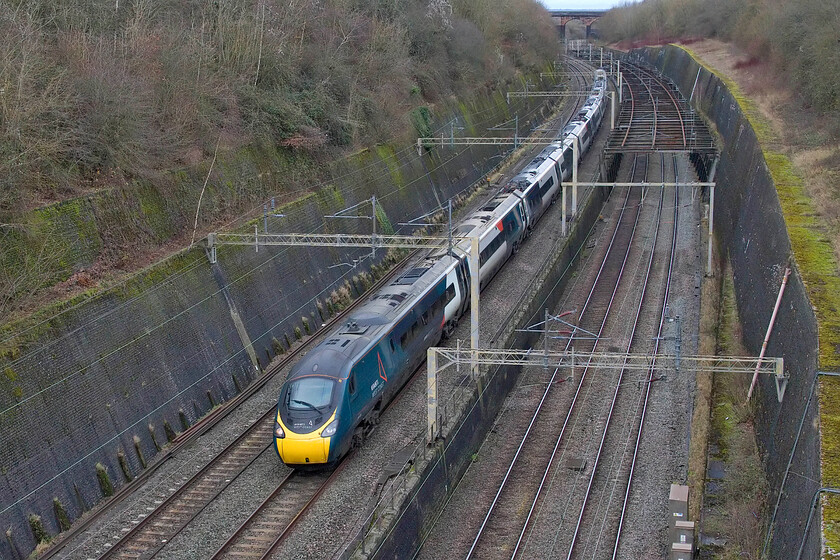 390104, VT 11.43 Liverpool Lime Street-London Euston (1A25, 3E), Roade cutting 
 390104 'Alstom Pendolino' works the 1A25 Liverpool to Euston service and is about to pass under Bridge 210 (Accommodation bridge) at the northern end of Roade cutting. The substantial wall and steel framework that spans the slow lines (known as the birdcage) was installed to prevent the collapse of the cutting following the disastrous events of the night of 13.11.1892 which saw a huge landslip. This saw the return to the area of up to two thousand navies to repair the damage and reopen the slow lines, a task that took some time as further slippage took place during this work. 
 Keywords: 390104 11.43 Liverpool Lime Street-London Euston 1A25 Roade cutting Alstom Pendolino AWC Avanti West Coast