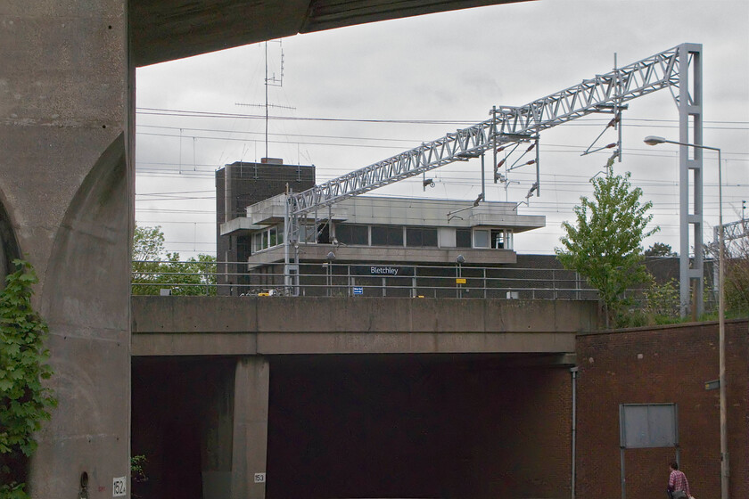 Bletchley PSB (BR, 1965) from Queensway 
 A concrete structure pictured from within a sea of other concrete structures! Just poking its head above the Queensway overbridge, which itself carries the WCML just to the south end of Bletchley station, is the closed and doomed (?) PSB. Just to my left and overhead is the flyover built by British Railways, as part of the modernisation plan to carry the Varsity Line over the WCML. This structure predates the 1965 PSB being built in 1959. Way ahead of its time, even by having concrete pads to support electrification masts, the viaduct saw very little use with the decline in coal traffic after its construction. However, there are plans to resurrect the east-west Varsity Line in some form or another so, maybe, it will see use once again. 
 Keywords: Bletchley PSB BR 1965 Queensway