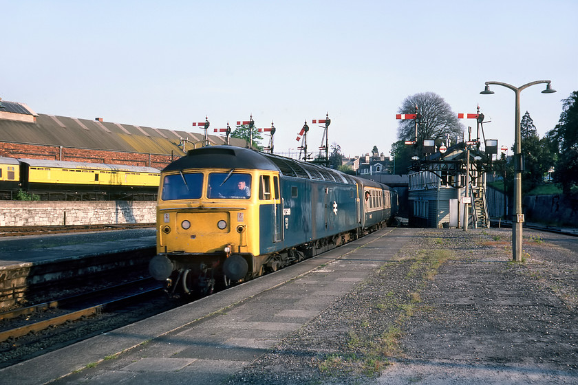 47549, unidentified up working, Newton Abbot station 
 47549 brings an unidentified up working into Newton Abbot station on the up relief line having just passed a fine array of GW lower quadrant signals and the West signal box. To the right of the train is the superb bracket holding two main dolls and two short dolls. There are some permissive reversing arms on the bracket along with a pair of route describers so that the backing drivers know where the signalman is sending them. The gantry to the left still exists today, but not over the railway line, but a stone's throw away from this location at the entrance to the appropriately named Brunel Road Industrial Estate. I took a photograph standing on about the same spot during a visit to the station in 2017, see..... https://www.ontheupfast.com/p/21936chg/24745328004/x43139-1c79-newton-abbot-station 
47549 had an interesting history as it was one of the three Class 47s that were marooned on Anglesey following the disastrous 1970 bridge fire and being repatriated by boat to Barrow-in-Furness. 
 Keywords: 47549 up working Newton Abbot station