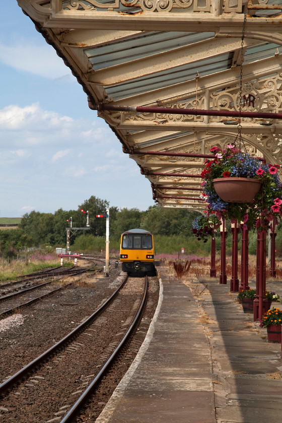 144022, NT 12.20 Leeds-Lancaster (2H13, 2L), Hellifield station 
 144022 leaves Hellifield station forming as the 12.20 Leeds to Lancaster. This train will diverge from the mainline at Settle Junction and head cross-country via Wennington towards the coast. Notice the well watered hanging baskets hung from the wrought ironwork that makes up the impressive canopies at Hellifiled station. 
 Keywords: 144022 2H13 Hellifield station