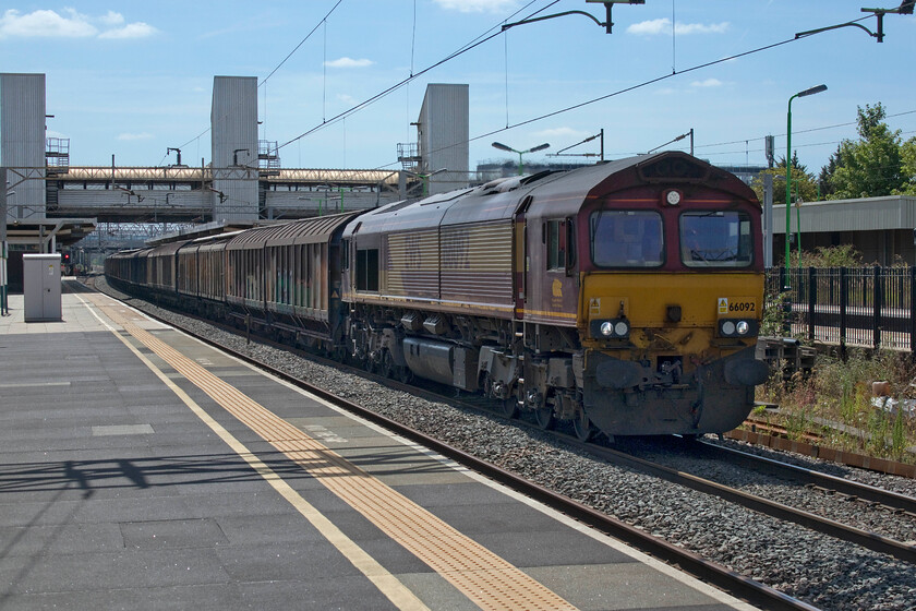 66092, 06.37 Dollands Moor-DIRFT (6M45, RT), Bletchley station 
 Despite looking directly into the midday sun and thus breaking all the rules in the photographic book a reasonable shot of 66092 has been secured at Bletchley station as it speeds northwards with the daily 6M45 06.37 Dollands Moor to Daventry bottled water train. Photoshop has once again earned its keep with a fair amount of layers and adjustments to get things dramatically better than its original RAW image. At least I managed an image that is more than Andy did standing next to me as he did not notice that his memory card was full until he went to compose the scene as 66092 approached and this was a Class 66 that he needed a photograph of! I did exactly the same last year, see.... https://www.ontheupfast.com/p/21936chg/30019701998/x37884-12-07-derby-rtc-wembley-hs 
 Keywords: 66092 06.37 Dollands Moor-DIRFT 6M45 Bletchley station water train EWS