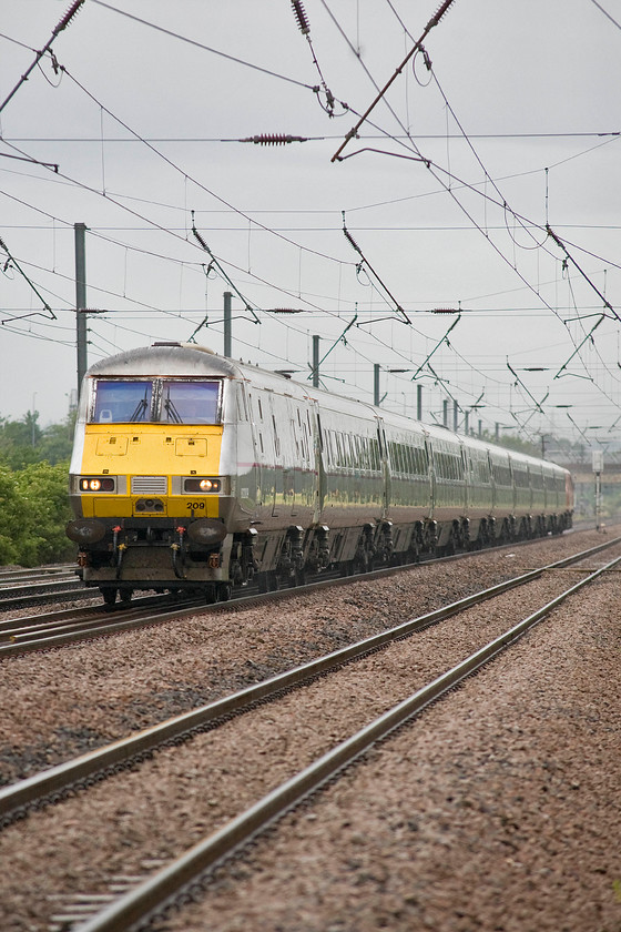 82209, GR 06.40 Leeds-London King`s Cross (1A06), Holme Green crossing TL192426 
 For a change, I like taking portrait photographs especially when using my trusty but infrequently used Sigma 80-200 zoom lens. As it was such a dull July morning I had to have the lens wide open at f4.0 that meant the depth of field was somewhat compromised even more so at 200mm meaning the track in the foreground was out of focus. However, a narrow depth of field often draws the eye to the subject as long as it is actually in focus itself! DVT 82209 leads the 06.40 Leeds to King's Cross past Holme Green crossing just south of Biggleswade. Note that the entire train is in the former operator's livery apart form the Class 91 on the rear that is in Virgin East Coast's bright new colour! 
 Keywords: 82209 06.40 Leeds-London King`s Cross 1A06 Holme Green crossing TL192426 DVT Virgin East Coast