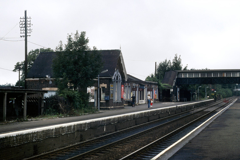 Harpenden Central station 
 On a quiet Sunday morning, a few people wait on the down fast platform at Harpenden Central station. These station buildings are all that remains of the station today and, in a way, it is surprising that they survived when the station has been so extensively developed over the years. Notice the trio of British Railways (LM) enamels adorning the front of the station and the rather unkempt nature of the platforms. 
 Keywords: Harpenden Central station