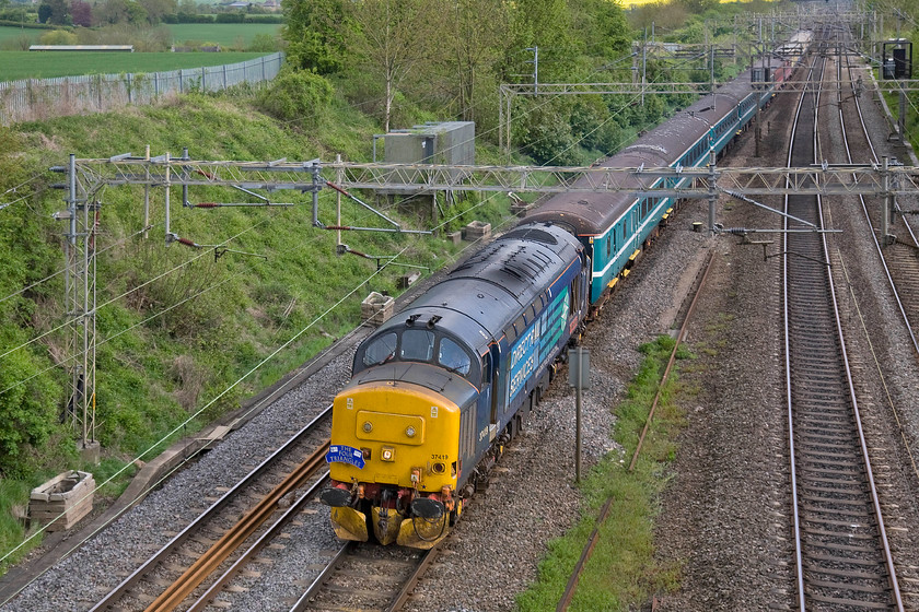 37419, 12.44 London Euston-Crewe (1Z46), Victoria bridge 
 With the stock having been used the previous day's (09.05.15) The Four Triangles railtour it is seen returning north past Victoria bridge just south of Roade. This was a one-way move running as 1Z46 that was supposed to leave Euston for Crewe at lunctime. However, by the time it reched this location, some sixty miles into its journey to Crewe, it was two hours late. Rather than running as empty coaching stock, passengers could pay a modest fare for the one-way journey travelling behind DRS' 37419 'Carl Haviland'. 
 Keywords: 37419 12.44 London Euston-Crewe 1Z46 Victoria bridge DRS 120 minutes late