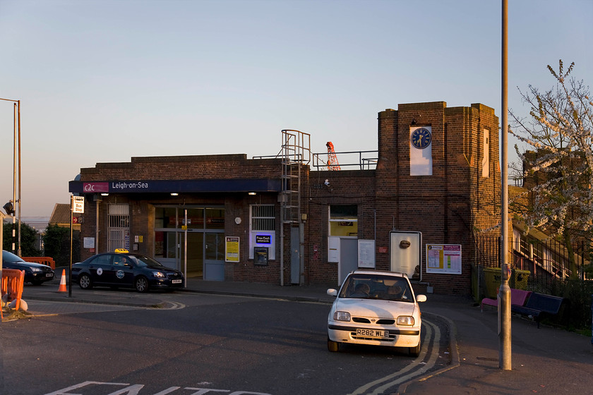 Frontage, Leigh-on-Sea station 
 The frontage of Leigh-on-Sea station just catches the late evening sunshine and marks our final stop for the day before heading for home in the white Nissan Micra parked up (quite illegally!) in the foreground. This is the second station building at Leigh replacing the earlier 1855 building in 1934 and built unashamedly in the style of the era. A notable feature is the four-sided clock tower with its white-painted stone inserts matched by a second one on the up (south) side of the station. . Notice the clear view of the north Kent coast across the Thames Estuary to the extreme left. 
 Keywords: Frontage Leigh-on-Sea station