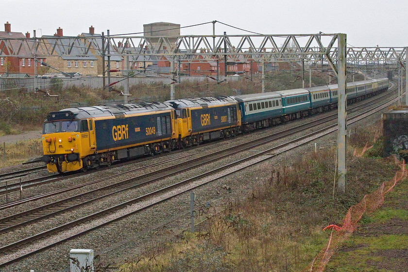 50049 & 50007, 09.25 Wembley Yard-Burton-ot-Wetmore Sidings ECS (5Z61, 81L), site of Roade station 
 50049 'Defiance' leads 50007 'Hercules' past the site of Roade station with the empty coaching stock from yesterday's jaunt to Manchester and Preston after its late-night return to Euston. Unfortunately, 50049 leading the 5Z61 09.25 Wembley Yard to Burton-ot-Wetmore working was powered right down at this point due to the train being right behind a local London Northwestern stopper service so the English Electric soundtrack was a little muted! 
 Keywords: 50049 50007 09.25 Wembley Yard-Burton-ot-Wetmore Sidings ECS 5Z61 site of Roade station GBRf Defiance Hercules