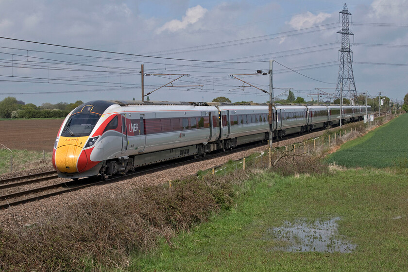 801024, GR 11.01 Edinburgh Waverley-London King's Cross (1E12, 1L), Joan Croft Junction 
 The closure of the level crossing a Joan Croft Junction in 2014 necessitated the construction of a large overbridge for the little traffic using the minor road linking the tiny village of Thorpe in Balne with the busy A19. Whilst the bridge is certainly not an attractive affair being built to Network Rail's latest standards its approach embankments do offer some superb views of the ECML. Taken from the east side of the bridge 801024 heads south with the 11.01 Edinburgh to King's Cross 1E12 LNER service. Just visible above the fourth carriage of the train to the left of the vast pylon is the steeple of the former All Saints Church in the tiny hamlet of Haywood. It is now a private residence very close to the ECML but what a place to live, see...... https://www.examinerlive.co.uk/news/local-news/inside-beautiful-church-transformed-stunning-19331791. Coincidentally, back in the summer of 1978 I camped near the hamlet while photographing Deltics on the ECML with Graham, see.... https://www.ontheupfast.com/p/21936chg/25410464804/campsite-haywood 
 Keywords: 801024 11.01 Edinburgh Waverley-London King's Cross 1E12 Joan Croft Junction LNER Azuma