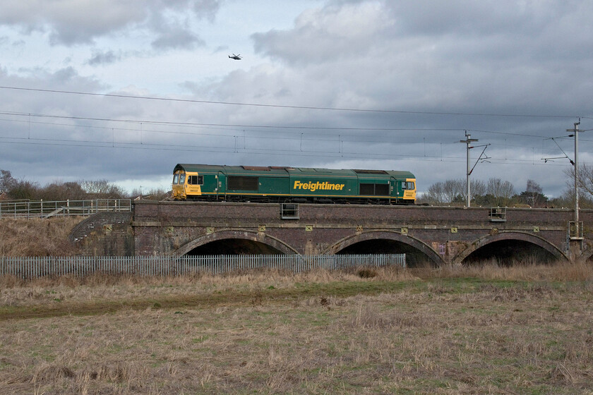 66522, 09.14 Southampton MCT-Garston (4M58, 38E), Kingsthorpe SP737635 
 As the sun puts in a welcome but half-hearted appearance on this very cold and windy afternoon 66522 climbs away from Northampton crossing Kingsthorpe Brook leading the ridiculously lightly loaded 4M58 09.14 Southampton to Garston Freightliner service. In fact, seven articulated lorries could have carried the entire contents of this train up the A34, the M40 and the M6 such was the dearth of boxes on-board! Above the train, having just taken off from nearby Sywell Aerodrome, is a charter operated Agusta-Westland AW169 helicopter with the call sign G-GETU that was making the relatively short trip to Bedford. 
 Keywords: 66522 09.14 Southampton MCT-Garston 4M58 Kingsthorpe SP737635 Freightliner Agusta-Westland AW169 Helicopter G-GETU