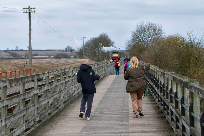 Carol & Charlie, walking back to Merry Tom Lane, crossing Bridge 13 
 My wife and son walk across Bridge 13 on the way back to Merry Tom Lane where the car is parked on this grey and cold Easter day. The Northampton and Lamport Railway's 12.30 return service can be seen in the distance heading back towards us with the exhaust from 2104 indicating a strong easterly wind was blowing and a cold one it was at that! 
 Keywords: Carol Charlie walking back to Merry Tom Lane crossing Bridge 13