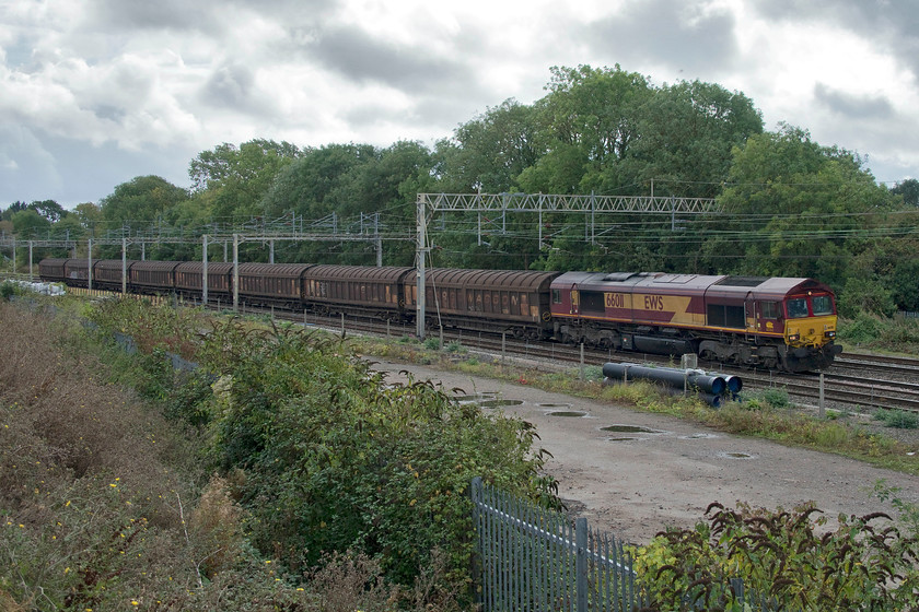 66011, 09.06 Dollands Moor-DIRFT (6C24), site of Roade station from former Pianoforte site 
 66011 leads a short train made up of cargo waggons is seen passing Roade taken from a new location created by the construction of a large bank associated with a large and new housing estate. 66011 is leading the 09.06 Dollands Moor to Daventry rail freight terminal carrying some sort of imported steel product. Looking at the menacing sky, it suggests that I am in for an imminent soaking, indeed I was within the next ten minutes! 
 Keywords: 66011 09.06 Dollands Moor-DIRFT 6C24 site of Roade station from former Pianoforte site