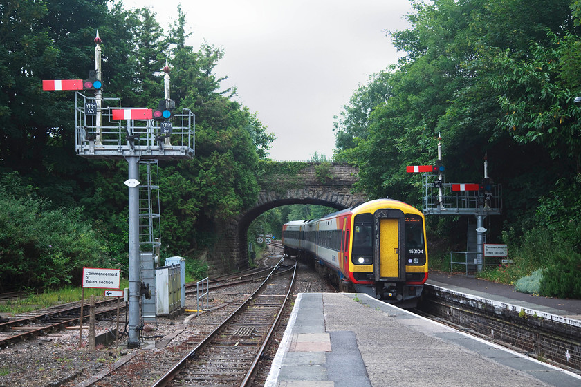 159104, SW 16.46 Yeovil Junction-London Waterloo (1O64, 2E), Yeovil Pen Mill Station 
 With mechanical signalling being wiped away in large swathes now, it is remarkable to find that Yeovil Pen Mill is still home to a mixture of lower and upper quadrant signals, a GWR box and absolute block. At the southern end of the station, 159104 arrives with an odd working, the 16.45 Yeovil Junction to Waterloo via Castle Cary. This working ran via this unorthodox route in order to serve passengers at the Glastonbury Festival who were bussed from the venue to and from Castle Cary station. Notice the cobbled together bracket signals here composed of new posts, ladders and railings with the old signal poles, complete with their finials, bolted on. This resignalling took place in April 2008. 
 Keywords: 159104 1O64 Yeovil Pen Mill Station