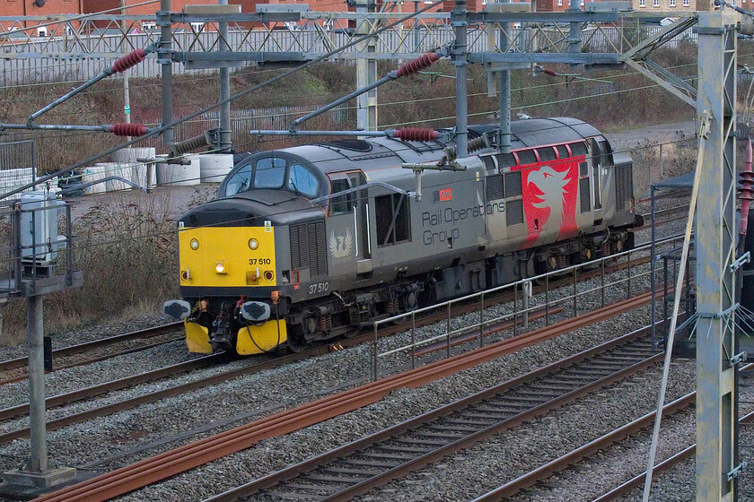 37510, 14.14 Wembley Yard-Derby RTC (0M57, 24E), site of Roade station 
 A quick search (using the search tool) of my website reveals that all of my photographs of ROG's 37510 'Orion' are of it running light engine! In another such move, it is seen passing Roade as the 0M57 14.14 Webley Yard to Derby RTC via a reversal at Nuneaton. I do not quite understand why these moves take this route rather than traversing the Marston Vale line to Bedford and then a quick run up the MML to Derby. 
 Keywords: 37510 14.14 Wembley Yard-Derby RTC 0M57 site of Roade station ROG Rail Operations Group Orion.