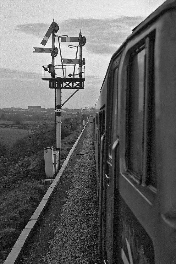 50044, 17.52 London Paddington-Westbury (1K68), Heywood Road Junction 
 The first of a sequence of photographs that I took from the leading droplight of the 1K68 17.52 Paddington to Westbury train as it approached its destination. My ability to take so many shots in close succession was due to me now having loaded an FP4 film in the camera provided by college rather than using my own supplied and very expensive Kodachrome 64! Looking into the evening light 50044 'Exeter' has just left the Westbury cut-off that is now curving away to the left out of sight and is about to pass the Heywood Junction home that is pulled off. The distant arm is Westbury North's and is still at danger meaning that our train will have to slow and even prepare to stop before it can enter the station probably caused by the train that can be seen crossing our path in the distance either leaving or arriving at Westbury travelling via the Avon Valley route. The two submissive arms on the shorter doll are for the chord that led to Hawkeridge Junction that at this time saw little use. A reverse angled photograph of this fine bracket signal can be seen taken the previous summer, see..... https://www.ontheupfast.com/p/21936chg/29513954004/x50041-18-35-london-paddington-newton 
 Keywords: 50044 17.52 London Paddington-Westbury 1K68 Heywood Road Junction Exeter