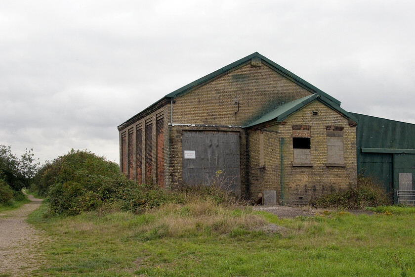 Former good shed, Twenty Feet River 
 Twenty Feet River is a large drainage channel that runs around the northern edge of the Fenland town of March. After leaving Whitemoor Yard the former GN & GE Joint line that once linked March with Spalding crossed Twenty Feet River with a level crossing immediately beyond the bridge. There was a crossing keeper's house but no station which made the construction of a substantial goods shed unusual. Today the goods shed is firmly secured and is adjacent to the well patronised footpath that follows the trackbed from here to Guyhirn which can be seen to the left. 
 Keywords: Former good shed, Twenty Feet River