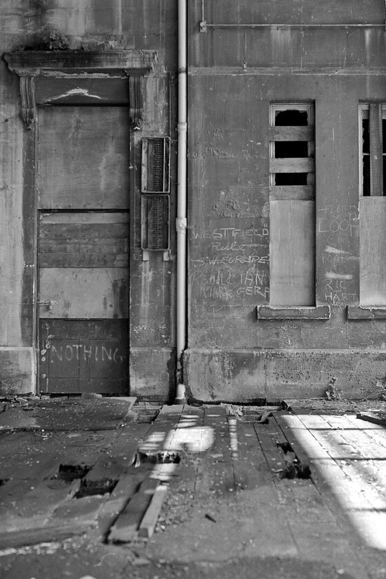 Main building from concourse, Bath Green Park station 
 Details of the Bath's Green Park station's main building are seen with the timber concourse in the foreground. The rotten timbers of the latter forced me to take great care while exploring the depths of the station. It always strikes me as odd that people seem to have an obsession with writing their respective names on walls of old buildings such as can be seen here. If this was today the walls would be adorned with masses of spray paint from the graffiti vandals who try to convince us that their actions are an art form. 
 Keywords: Main building from concourse Bath Green Park station