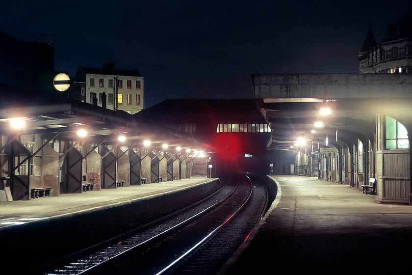 Kentish Town station 
 A time exposure taken at Kentish Town station looking north-west away from St. Pancras. At this time, the station was looking a little tired being in need on renovation and modernisation, something that happened when the line was electrified in the next couple of years. Notice the benches in the alcoves along the length of the platforms. Also, notice the banner repeater signal on the down platform due to poor sighting caused by the sharp left-hand curve. A look at Google earth reveals that the two buildings above the station are still extant. The one with the turret to the right is The Assembly House pub and featured in my 2020 attempted recreation of the same scene, see..... https://www.ontheupfast.com/p/21936chg/28800885404/kentish-town-station 
 Keywords: Kentish Town station