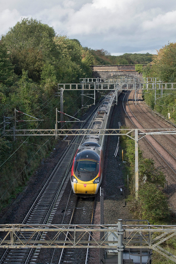 390135, VT 11.36 Manchester Piccadilly-London Euston (1A20, 20L), A508 road bridge 
 After the rain, the sun put in an appearance, just enough to illuminate the southern end of Roade cutting. 390135 'City of Lancaster' (only named on one side) catches the sun woking the 1A20 11.36 Manchester Piccadilly to Euston. I love the lighting in this image with the rain leaden sky and the trees and foliage beginning to take on its autumn glow. 
 Keywords: 390135 11.36 Manchester Piccadilly-London Euston 1A20 A508 road bridge