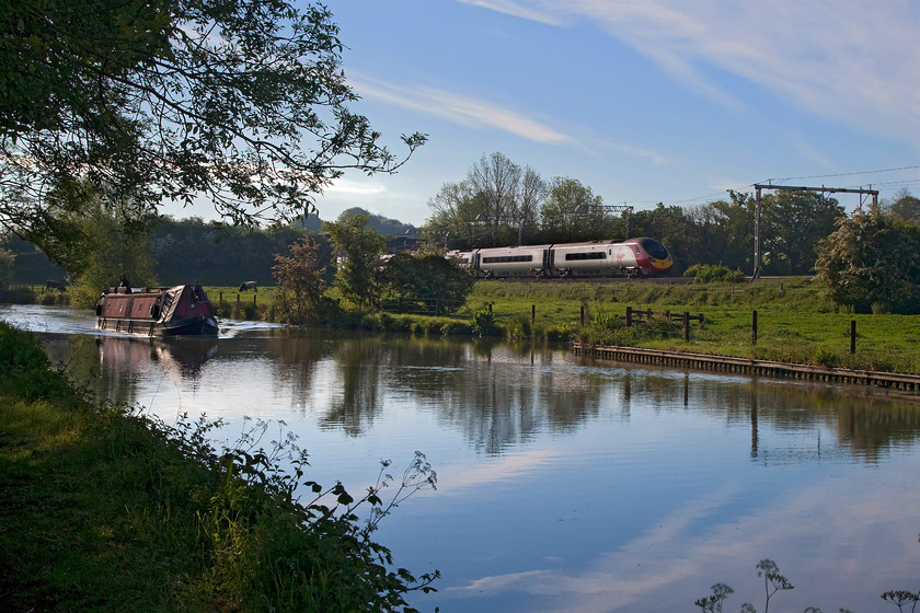 390132, VT 06.27 Wolverhampton-London Euston (1B03, RT), Bugbrooke SP679564 
 Two technologies from totally different eras pass near Bugbrooke in Northamptonshire. A narrow boat makes its leisurely way along the Grand Union Canal disturbing the completely still water whilst 390132 'City of Birmingham' storms south forming the 06.27 Wolverhampton to Euston. 
 Keywords: 390132 1B03 Bugbrooke SP679564