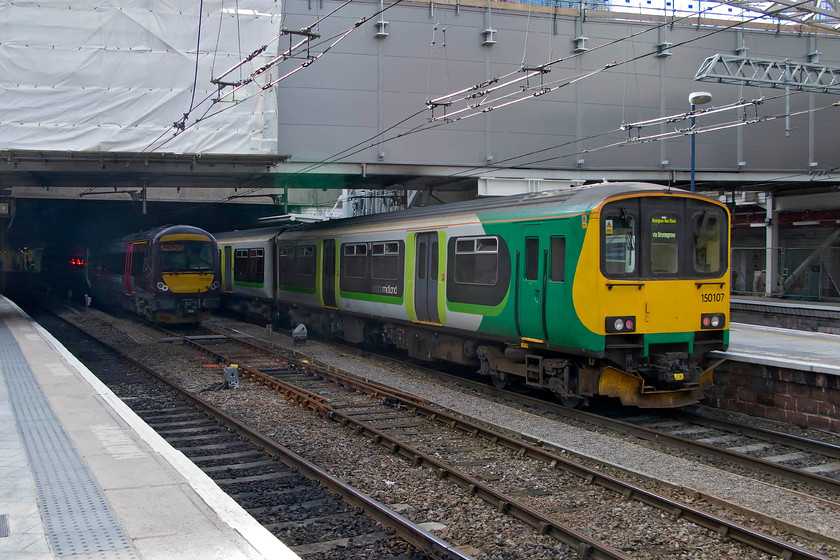 150107, LM 07.34 Hereford-Birmingham New Street (1M57) & 170520, stabled, Birmingham New Street station 
 There is plenty of evidence in this photograph of the protracted reconstruction of Birmingham New Street station what with the sheeted off area and the barriers off to the extreme right. This much-awaited re-building is due to open very soon with things hopefully getting back to normal. 150107 brings the rear of the 07.34 from Hereford into the station where it will terminate. meanwhile, Crosscountry's 170520 is stabled in the centre road. 
 Keywords: 150107 07.34 Hereford-Birmingham New Street 1M57 170520 Birmingham New Street station