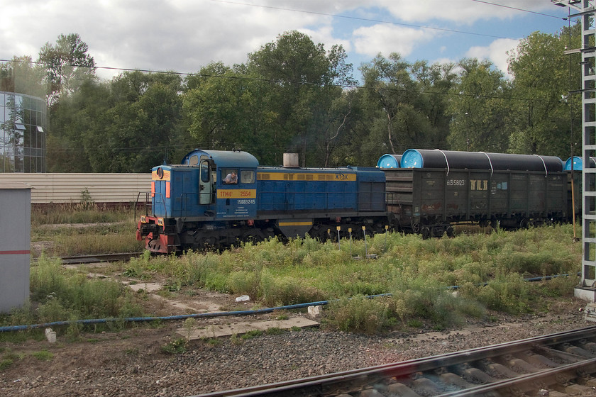 TGM4-2554, shunting, Kolpino steel works 
 One of the older generation of shunters, TGM4-2554, is seen from the train in the exchange sidings at Kolpino steelworks to the South of St. Petersburg. Now painted in a blue livery indicates that it is privately operated as many of this class of shunter now are. The generous loading gauge on Russian railways allows the huge wagons, as seen behind the shunter, to be conveyed. 
 Keywords: TGM4-2554 Kolpino steel works