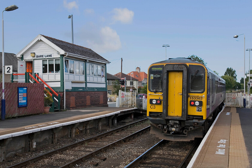 153363, NT 10.04 Lancaster-Morecambe, Bare Lane station 
 153263 departs from Bare Lane station, passing the 1937 LMS box, working the 10.04 Lancaster to Morecambe Northern service. The 'signalman' observes the passage of the train as it crosses the busy level crossing. However, when I say signalman he is in point of fact an employee of Northern Trains who is standing in as a station announcer and observer of goings on. The box was shut on 08.12.12 following a new crossing being installed with control passing to Preston PSB. Notice that the train appears to be running wrong line. This is because the two parallel bi-directional tracks are operated from Morecambe South Junction as 'long sidings'. The one to the right to Morecambe and the one to the left is freight only to Heysham for access to the nuclear power station. 
 Keywords: 153363 10.04 Lancaster-Morecambe Bare Lane station Northern