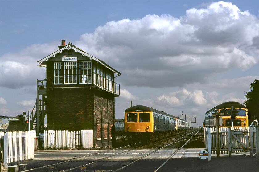 Class 105 & Class 101 DMU, 14.05 Peterborough-Cambridge & 47830, March East Junction 
 The 14.05 Peterborough to Cambridge DMU service leaves March passing the East Junction signal box. The train is made up of a two-car Class 105 and a three-car Class 101 unit leading. Both of these classes were found widely throughout East Anglia the former units being the first to succumb when withdrawals began following a number of them moving to the Northwest. No heat 47380 stands stabled to the right of the image that ended its life as a petroleum sector locomotive eleven years after this superb scene at March. 
 Keywords: Class 105 Class 101 DMU 14.05 Peterborough-Cambridge 47830, March East Junction first generation DMU