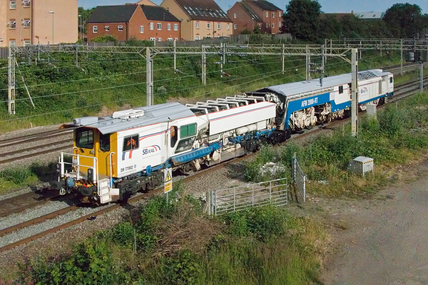 DR770002, 07.21 Northampton Castle Yard-Bletchley Flyover (6J99, 12L),site of Roade station 
 SB Rail's UNIMAT 09-44/4S DYNAMIC (to give it its full name) passes the site of Roade station in the bright early morning sunshine running as 6J99. It was making the relatively short trip from Northampton Castle Yard to Bletchley flyover where it would no doubt be put to use on the East-West Rail Link. 
 Keywords: DR770002 07.21 Northampton Castle Yard-Bletchley Flyover 6J99 site of Roade station SB Rail UNIMAT 09-44/4S DYNAMIC