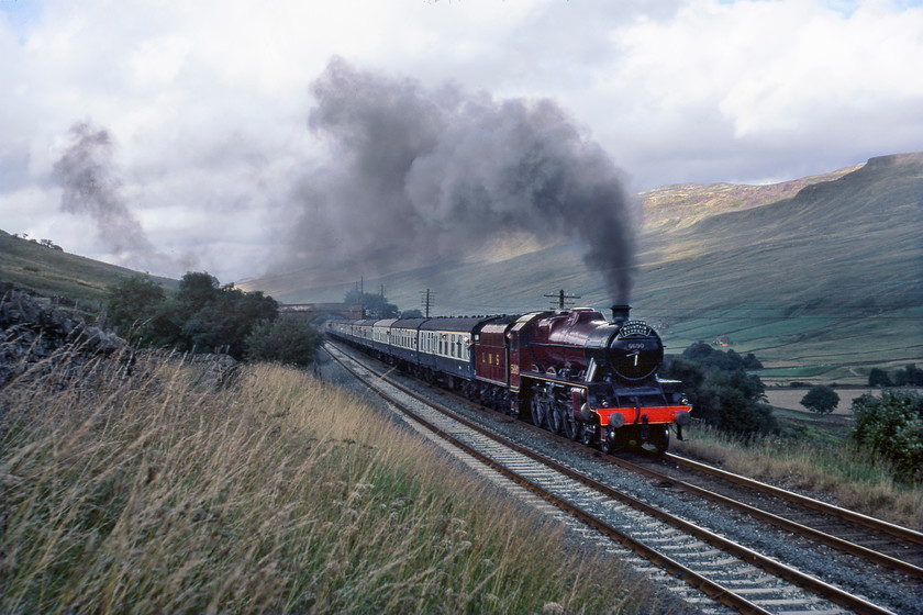 5690, outward leg of Cumbrian Mountain Express, Ais Gill SD773979 
 Having done its duty by rescuing a failed freight (hauled by 40179) consequentially now running very late 5690 'Leander' charges up the northern side of the Long Drag approaching Ais Gill summit near the hamlet of Angrholm. It is leading the outward leg of the BR organised Cumbrian Mountain Express. Leander's job will have been made more tricky by it having to make a standing start some five miles north of this location on the rising 1:100 gradient, the dark exhaust evidence of this; the recording is quite dramatic too at..... https://youtu.be/DZCJjc--QqM 
 Keywords: 5690 outward leg of Cumbrian Mountain Express Ais Gill SD773979