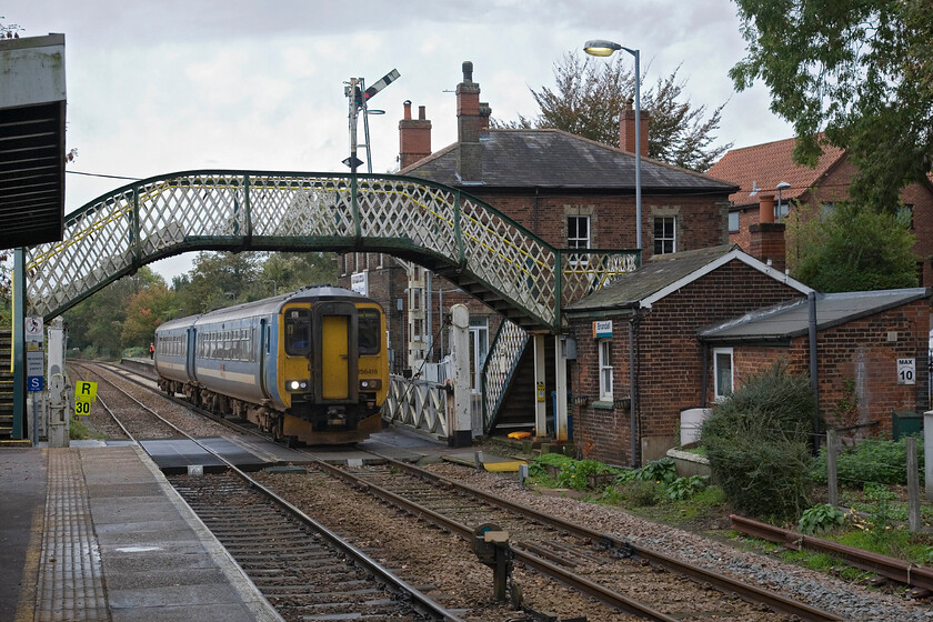 156416, LE 12.36 Norwich-Great Yarmouth, Brundall station 
 156416 'Saint Edmund' rattles through Brundall station working the 12.36 Norwich to Great Yarmouth service. It has just passed the superb home signal mounted on a rather grand and oversized post. The latticed footbridge is a typical design for the region with the manually operated gates and the associated crossing keeper box also of interest. I am not sure as to how many years of operation this superb infrastructure has left but plans are now afoot to resignl the lines east of Norwich so get your photographs whilst you can! 
 Keywords: 156416 12.36 Norwich-Great Yarmouth Brundall station Greater Anglia GA Saint Edmund