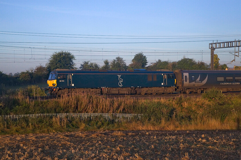 92010, CS 20.45 Inverness, 21.43 Aberdeen & 19.50 Fort William (1M16, 3L), between Roade & Ashton 
 With the rising sun just giving enough light, the 'Highland' sleeper is seen passing between Roade and Ashton. A smartly turned out 92010 leads a decidedly dirty and work-stained set of stock forming the 20.45 Inverness/21.43 Aberdeen and 19.50 Fort William 1M16 sleeper with its passengers beginning to stir with just forty-five minutes before arrival into Euston. I was glad of the sun on my back as it was a really chilly start to the day with a little grass frost. 
 Keywords: 92010 20.45 Inverness 21.43 Aberdeen 19.50 Fort William 1M16 between Roade & Ashton Caledonian Sleeper